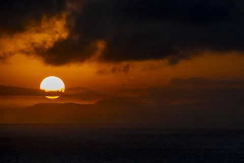 Dramatic sunset over the ocean with fiery orange clouds and dark sky Photos