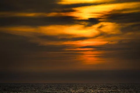 Dramatic sunset over the ocean with fiery orange clouds and calm water Fotos de archivo