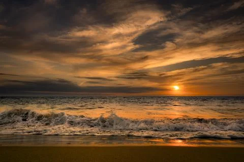 Dramatic sunset over the ocean with fiery clouds and crashing waves on the .. Photos