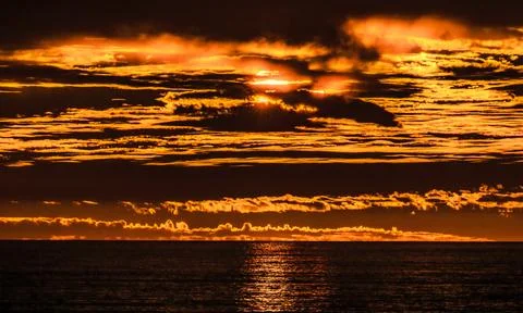 Dramatic sunset over the ocean with fiery orange clouds and shimmering wate.. 스톡 사진