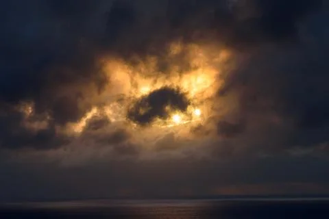Dramatic sunset over ocean with golden sunlight breaking through dark storm clou Stock Photos