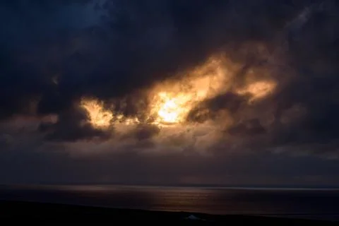 Dramatic sunset over ocean with golden sunlight breaking through dark storm clou Stock Photos