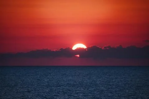 Dramatic sunset over the ocean horizon at dusk with clouds partly covering .. Stock Photos