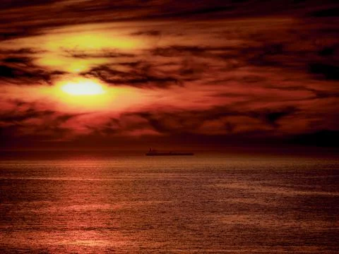 Dramatic sunset over the ocean with a lone cargo ship on the horizon Foto stock