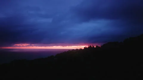 Dramatic Sunset Over Ocean with Silhouetted Hillside and Stormy Clouds. Stock Footage 338360676