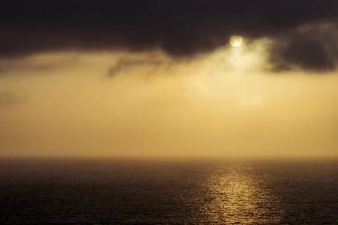 Dramatic sunset over the ocean with sun peeking through dark clouds Fotos de archivo