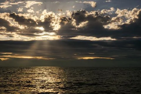 Dramatic sunset over the ocean with sunbeams breaking through dark clouds 库存照片
