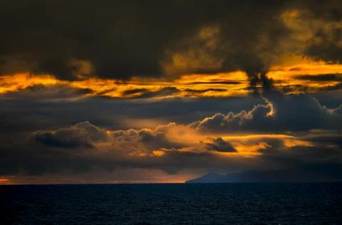 Dramatic sunset over the ocean with vibrant clouds and distant mountains Photos