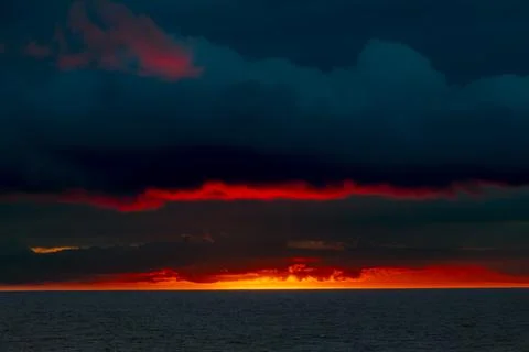 Dramatic sunset over the ocean with vibrant red clouds and dark sky 库存照片