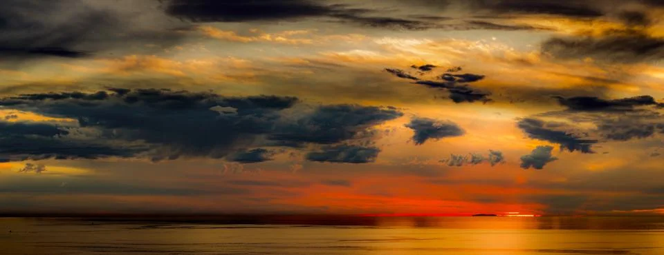 Dramatic sunset over the ocean with vibrant orange and dark clouds Stock Photos