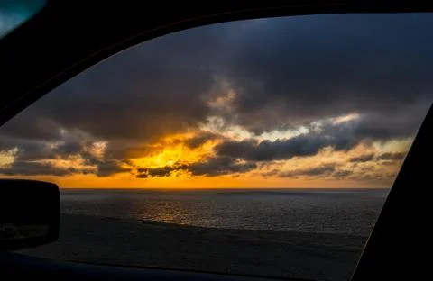 Dramatic sunset over the ocean viewed through a car window 库存照片