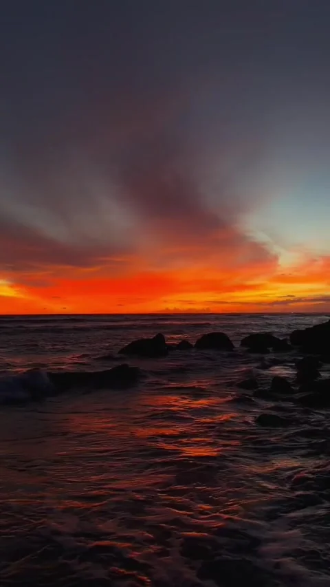 Dramatic sunset over ocean waves with rocky shoreline and vibrant orange sky Vídeos de archivo 334084962