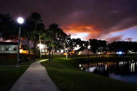 Dramatic Sunset Over Palm Trees and Park Pathway with Streetlights Stock Photos