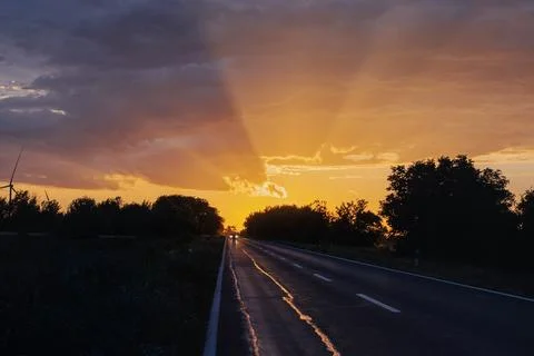 Dramatic sunset over the road after the storm with car coming from the distance Stock Photos