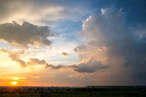 Dramatic sunset over rural area with stormy puffy clouds lit by orange settin Stock Photos