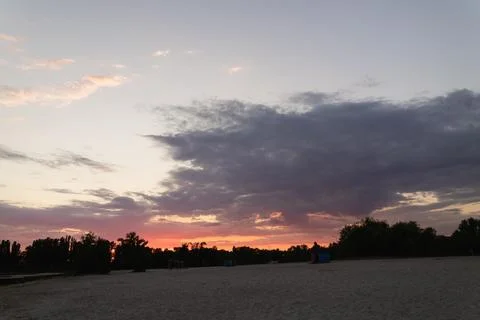 Dramatic sunset over a sandy beach with silhouetted trees and clouds Stock Photos