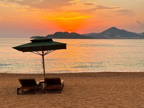 Dramatic sunset over the sea and empty chaise lounges on the beach Stock Photos