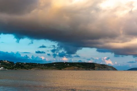 Dramatic sunset over sea water with gray clouds and sun lights Stock Photos
