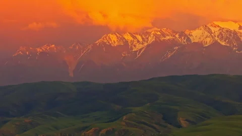 Dramatic sunset over snow-capped mountains and green foothills in Kyrgyzstan Stock Footage 326660313