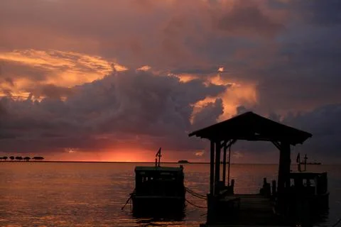 Dramatic sunset over tranquil ocean with boats docked at wooden pier Stock Photos
