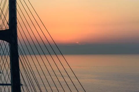 A dramatic sunset over a vast body of water with a modern cable-stayed brid.. Stock Photos