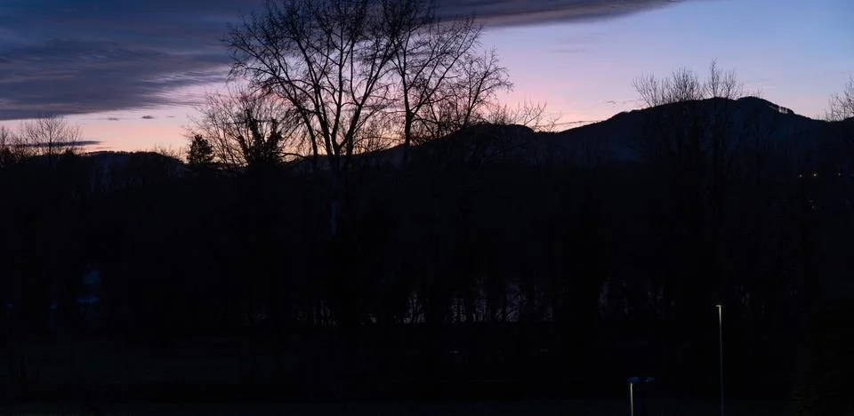 Dramatic sunset with pink blue clouds over bar trees and hills in wintertime Stock Photos