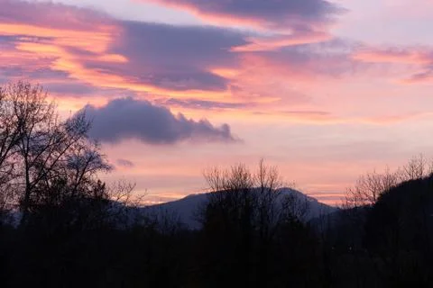 Dramatic sunset with pink clouds over bar trees and hills in wintertime in Sw Stock Photos