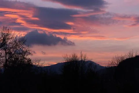 Dramatic sunset with pink clouds over bar trees and hills in wintertime in Sw 스톡 사진