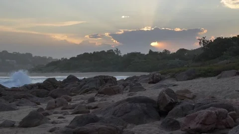 Dramatic sunset rays pierce through clouds over a rocky beach shoreline. Stock Footage 333363703