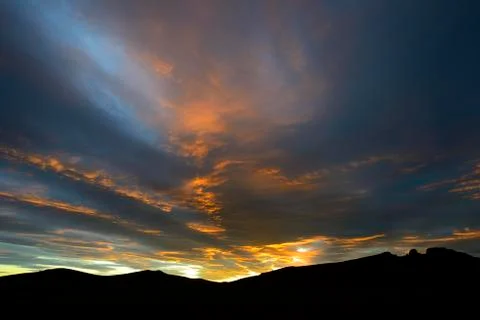 Dramatic sunset with rising storm clouds in front of mountain silhouette Pali Stock Photos