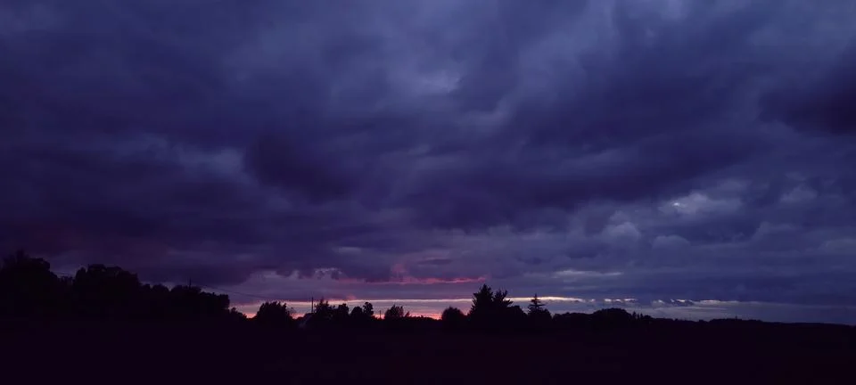 A Dramatic Sunset Scene with an Overcast Sky Featuring Silhouetted Trees in the Stock-Fotos