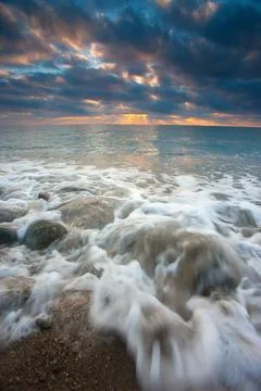 Dramatic Sunset Seascape with Pebbles and Foamy Waves Stock-Fotos