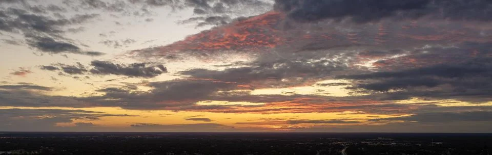 Dramatic sunset sky covered with colorful yellow clouds over dark ground. Pan Stock Photos