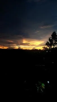 A dramatic sunset sky with dark clouds and warm golden light silhouetting tre Stock Photos