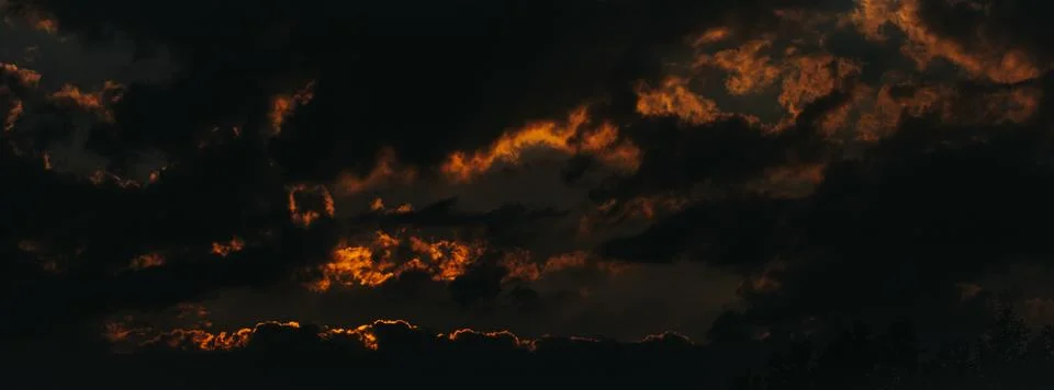Dramatic sunset sky with dark clouds and vibrant orange and yellow hues ill.. Stock Photos
