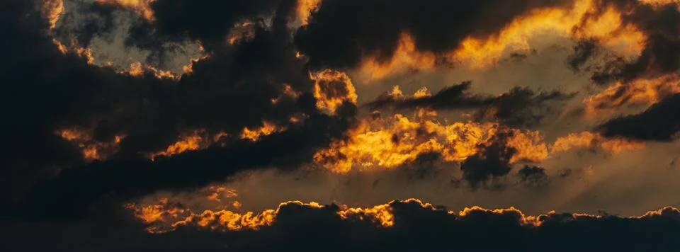 Dramatic sunset sky with dark clouds and vibrant orange and yellow hues ill.. Stock Photos
