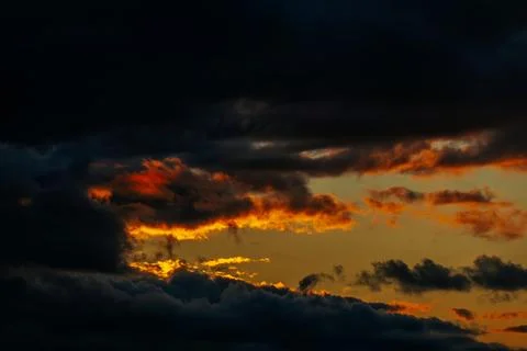 Dramatic sunset sky with dark clouds and vibrant orange and yellow hues ill.. Stock Photos