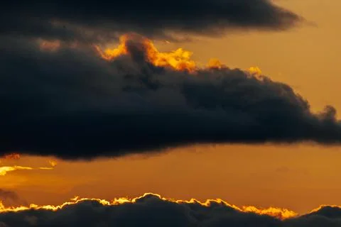 Dramatic sunset sky with dark clouds illuminated by orange and yellow hues,.. Stock Photos
