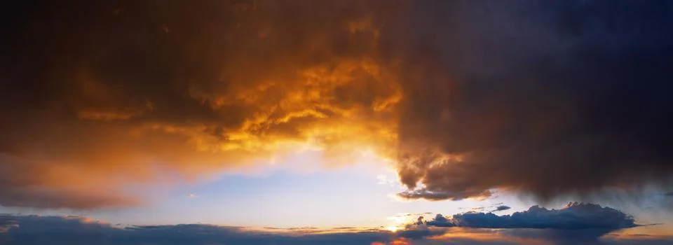 Dramatic sunset sky with dark rainy clouds illuminated with sun. Stock Photos
