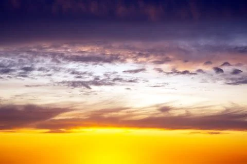 Dramatic sunset sky featuring golden, fiery clouds against a deepening blue.. Stock Photos