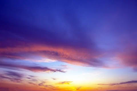 Dramatic sunset sky featuring golden, fiery clouds against a deepening blue.. Stock Photos