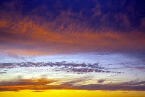 Dramatic sunset sky featuring golden, fiery clouds against a deepening blue.. Stock Photos
