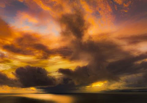 Dramatic sunset sky with fiery orange clouds over a calm ocean horizon Stock Photos