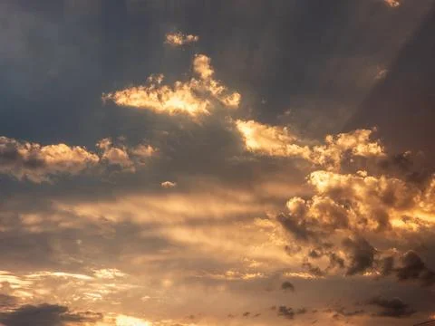 Dramatic sunset sky with golden sunbeams piercing through textured clouds Stock Photos