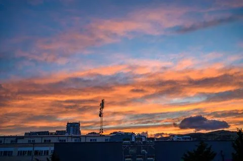 Dramatic sunset sky illuminates urban landscape with buildings and communic.. Photos