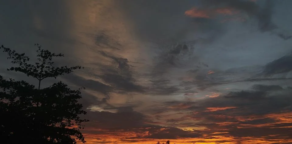 Dramatic sunset sky with orange and golden glow behind dark storm clouds Stock Photos