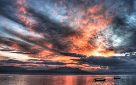 Dramatic Sunset Sky Over Calm Water and Mountain Silhouettes Stock Photos