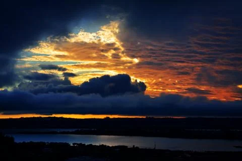 Dramatic sunset sky over dark waters of sea bay. Stock Photos