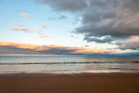 Dramatic sunset sky over the sea as waves gently lap onto the beach in the go Stock Photos