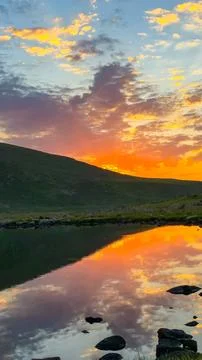 Dramatic sunset sky reflection in calm mountain lake at dusk Stock Photos